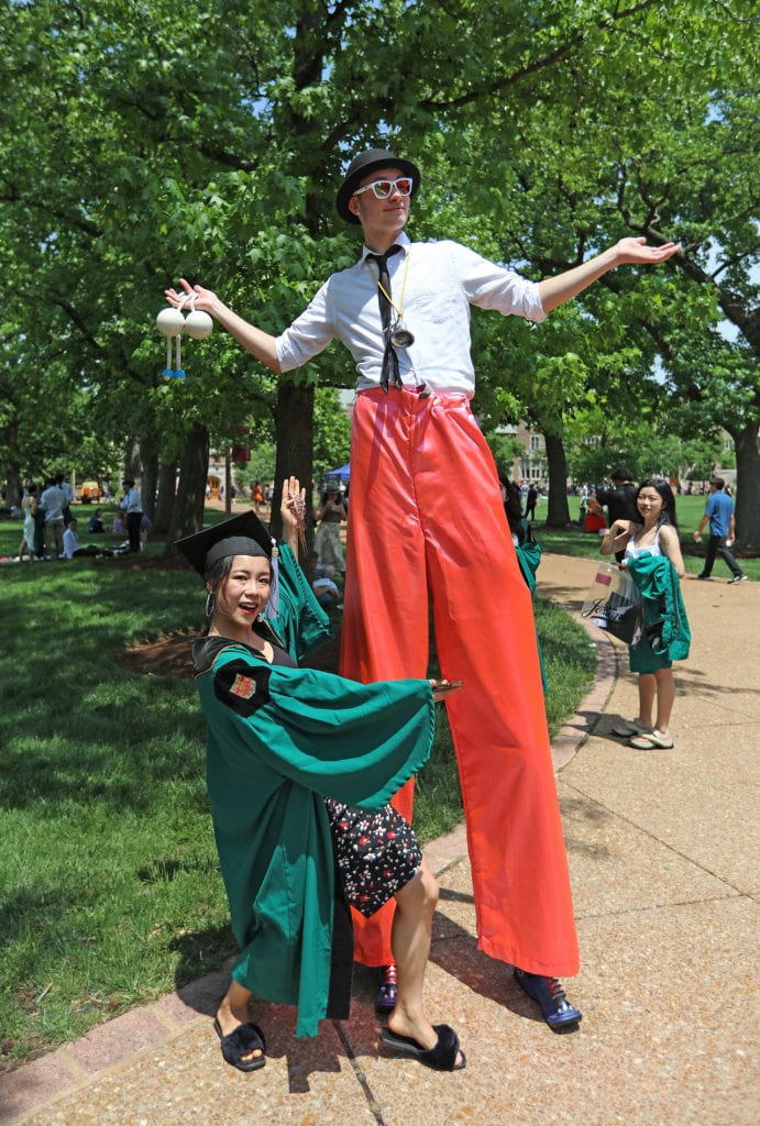 A WashU graduate poses next to a man on stilts.